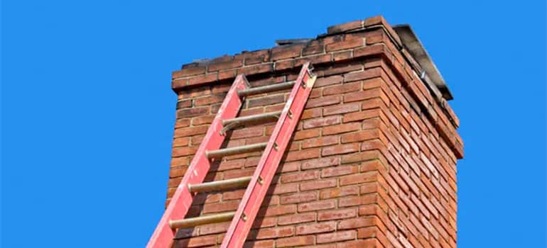 Ladder going up brick chimney for repair with blue sky in Sterling Heights MI