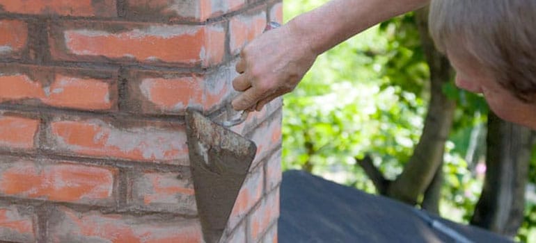 Closeup of man with trowel finishing chimney repair masonry work.